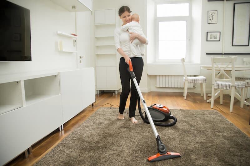 happy mother holding baby and vacuuming