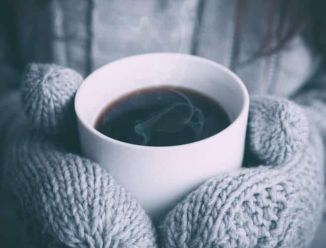 Cup of steaming black coffee held in woollen mits